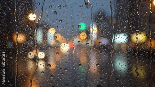 Raindrops falling on window glass close up blurred city street night lights bokeh background rainy weather condition moody autumn evening cozy water drops abstract macro shot stock video footage 4k hd