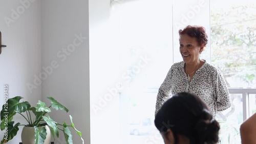 Smiling Mature Woman Walking Near Window with Houseplants at Home