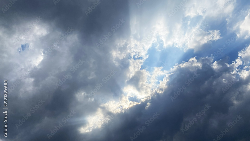 Obraz premium Dramatic sun rays breaking through dark heavy grey clouds