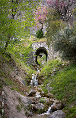 Small Mountain Waterfall Flowing Beneath a Stone Bridge in Spring, Italy