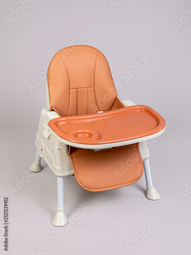 Dark orange baby high chair with tray on grey background