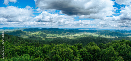 A panoramic view of green forests and hills under a cloudy sky. Bieszczady Mountains. View from the observation tower on Jeleniowaty.