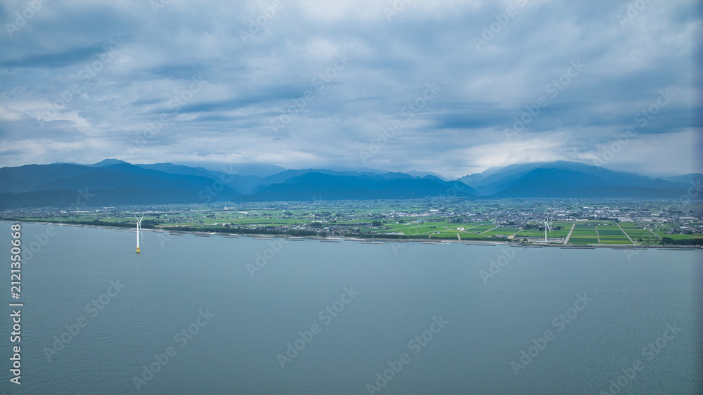 Fototapeta premium 梅雨明け前で高気温、高湿度の富山県下新川海岸の洋上風力発電風車や笹川地区や、さらに東側の糸魚川市の山の様子など
