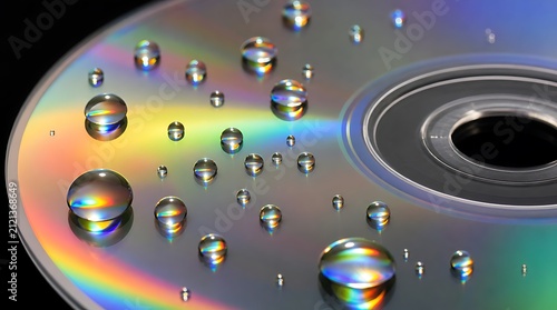 Macro water droplets on iridescent optical compact disc surface highlighting rainbow light reflection and liquid texture