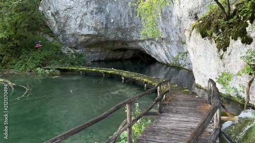 Rastovaca, Croatia - October 06, 2025: Plitvice Lakes National Park. Scenic wooden bridge leads to cave entrance over tranquil green water in lush forest setting