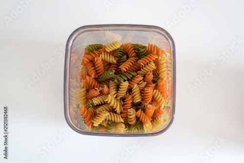 Foto Tri-color fusilli pasta in transparent plastic storage container top view isolat