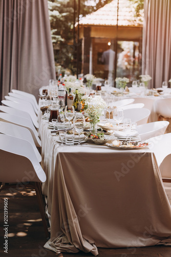 Long Banqueting Table Decorated with Flowers and Elegant White Chairs in Summer Restaurant