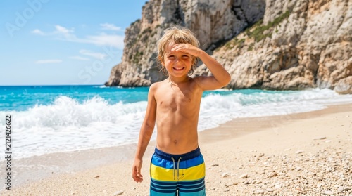 Happy young boy smiling on a sunny beach with ocean waves.