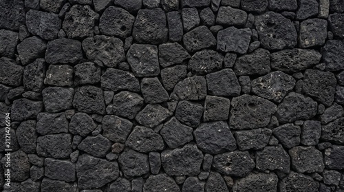 Dark Stone Wall Texture: A rugged and weathered dark stone wall, composed of irregularly shaped, charcoal-colored rocks, creates a visually striking and textured background.