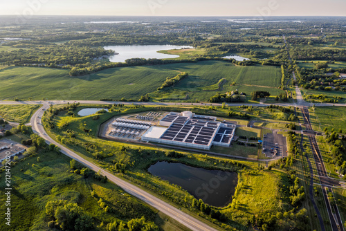 Aerial view of data center facility with solar panels on the roof, surrounded by green fields, ponds, and a winding road 