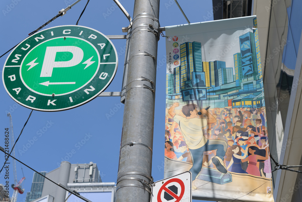 Fototapeta premium downtown Toronto pole-mounted projecting banner with round Municipal Parking sign on a blue sky in summer