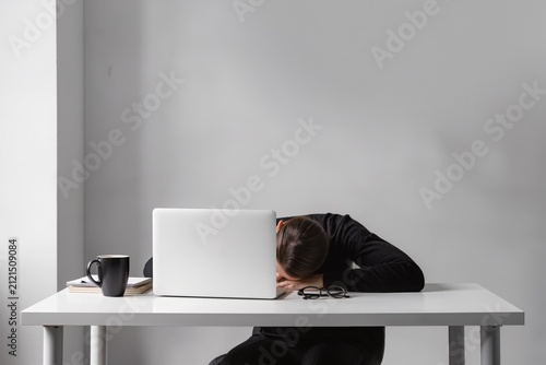 Employée épuisée endormie sur son bureau devant un ordinateur portable, concept de burn-out, surcharge de travail, fatigue professionnelle et stress au travail