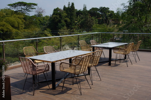 Outdoor restaurant terrace with rattan chairs and marble tables overlooking lush green forest view