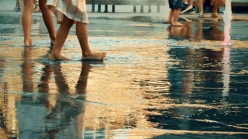 Barefoot children running and splashing through a shallow urban fountain on a warm summer evening