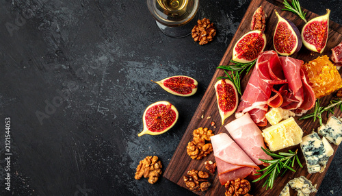 Charcuterie board with figs, cured meat, cheese, walnuts on dark wood serving plank