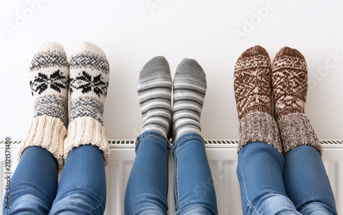 Family warming legs on heating radiator near white wall, closeup