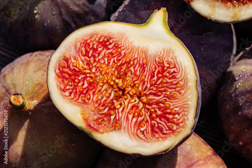 Fresh whole figs arranged with halved fruits. Juicy ruby interior. Seasonal Ficus carica harvest, antioxidant-rich nutrition, gourmet ingredients and Mediterranean healthy lifestyle.