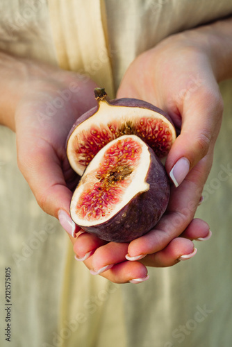 Woman presenting sliced ripe figs in hands, revealing their vibrant ruby flesh. Fresh Ficus carica fruit, organic harvest, healthy eating, gourmet ingredients and Mediterranean lifestyle