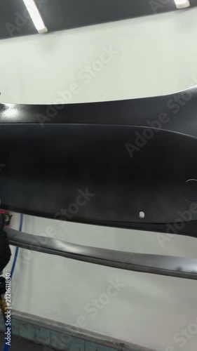 Professional auto body painter applying primer to a car bumper with spray gun