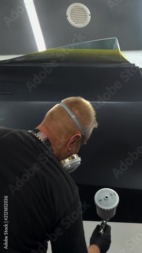 Professional auto body painter applying finish coat in a clean spray booth