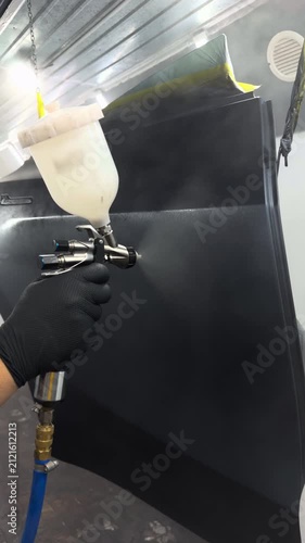 Professional auto body painter applying dark primer to a car door in a spray booth