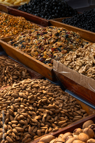 Colorful assortment of granola, dried fruits, almonds, walnuts, raisins and healthy snacks displayed in wooden trays at an outdoor market. Ideal for healthy eating, nutrition, organic food and retail 