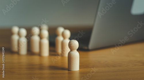 Foto Single wooden figure stands apart from a blurred group near a laptop