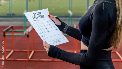 Fotografie Woman holding a 30-day fitness challenge tracker at a running track