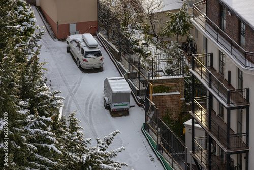 Snow covered the house territory and a car with a trailer. Snowfall and a snow-covered courtyard in cool weather. Winter weather.