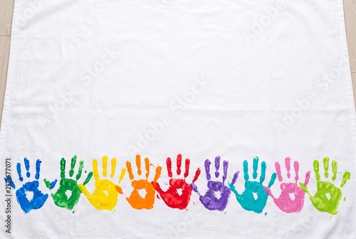 Colorful children s handprints form a rainbow border at the bottom of a white fabric, leaving generous blank copy space above. Playful background for education, inclusion, crafts, and campaigns.