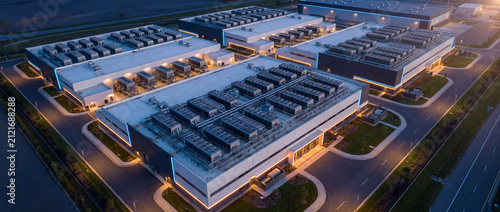 Data center building complex at dusk with aerial perspective shows modern architecture, rooftop HVAC cooling equipment, and LED lighting for cloud storage technology concepts
