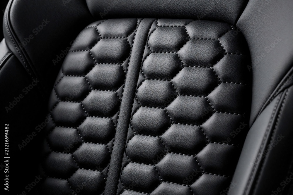 Obraz premium Black leather car features hexagonal quilting pattern. Close-up view of textured upholstery inside luxury vehicle. High-quality auto interior detail.