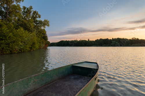 фотографія Old green metal rowboat anchored on a fish breeding pond at sunset
