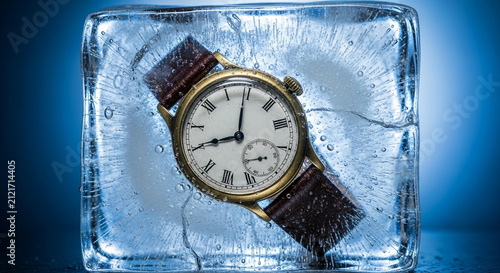Vintage wrist watch frozen inside a solid block of ice against a blue background