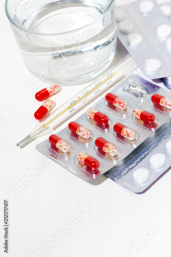 medicines in tablets and capsules, a thermometer and a glass of water, vertical