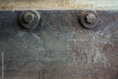 Two heavy hex bolts with washers mounted on weathered rusty metal plate surface of industrial machinery casing.
