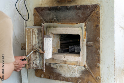 Man opening thick insulated door of industrial muffle furnace, revealing inner heating chamber with elements in a production workshop.