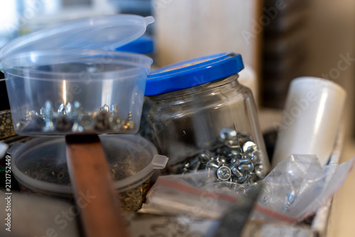 Foto Transparent plastic containers filled with various metal screws, self-tapping screws, and small hardware fasteners stacked on a home workshop shelf