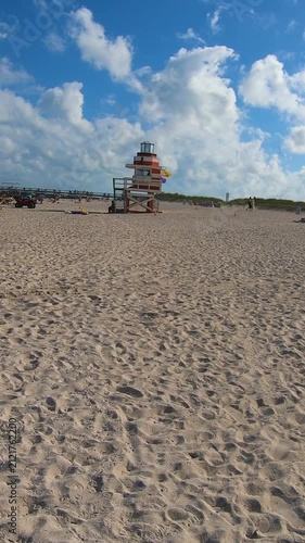 Vertical POV walk across Miami Beach toward a colorful lifeguard tower with sandy shoreline, ocean waves and the iconic Florida coastal atmosphere.