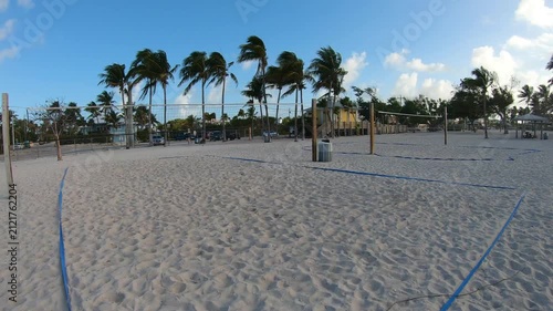 Vertical POV walk toward beach volleyball courts at Sombrero Beach in Florida at sunrise with golden light, palm trees and a tropical coastal atmosphere.