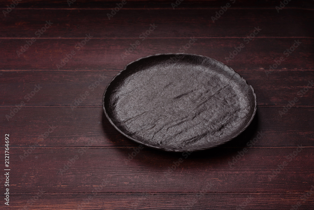 Obraz premium An empty round ceramic plate on a dark, textured brown background. An empty round plate