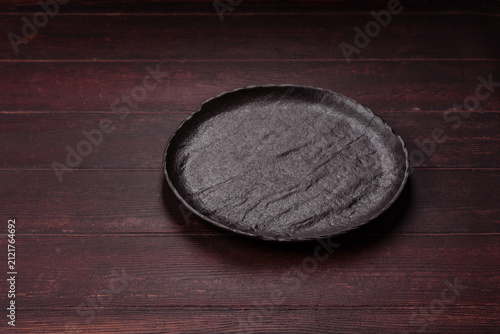 An empty round ceramic plate on a dark, textured brown background. An empty round plate