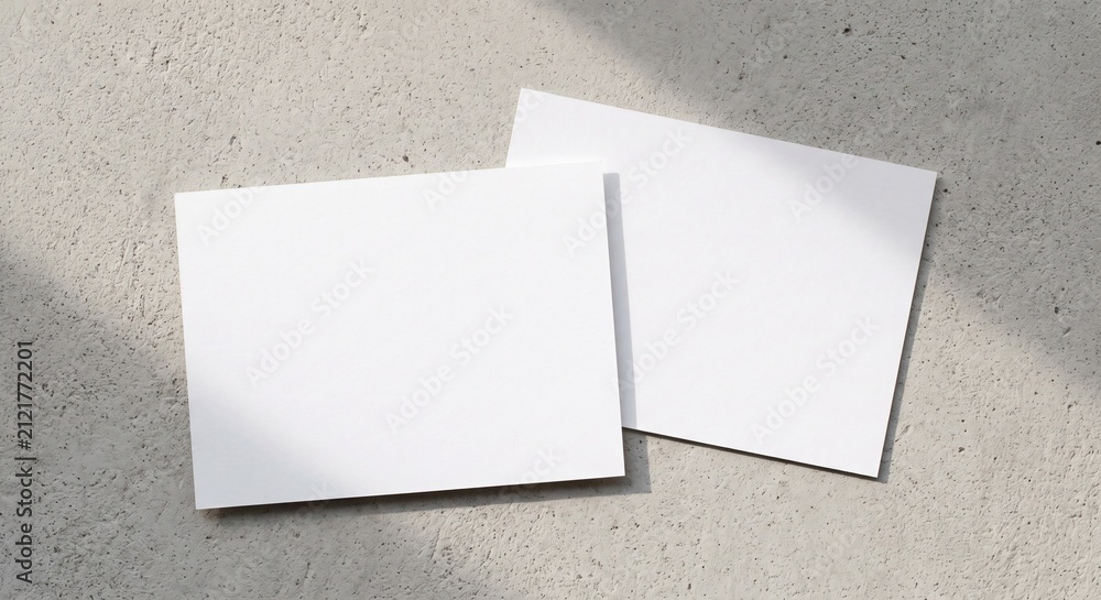 Fototapeta premium Top view of two blank white rectangular postcards on a light grey concrete background with soft shadows for stationery branding design.