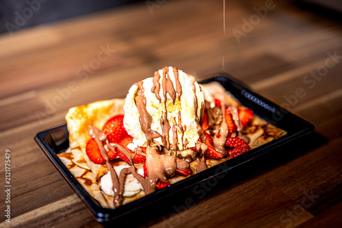 Freshly baked crepe and waffel with ice cream, chocolate and berries on wooden table. Served with spoon. Filled pancakes with strawberries, fresh berries and sauce.