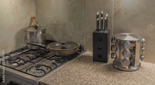 Фотография Close-up of a modern kitchen countertop featuring a black wooden knife block, a rotating stainless steel spice rack, and a gas stove with cookware
