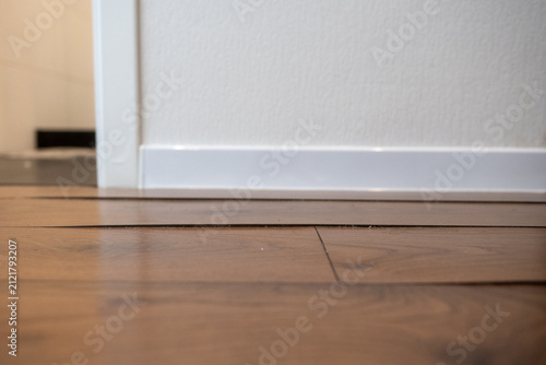 swollen laminate seam between two wood-grain planks in a hallway near the bathroom, vertical framing