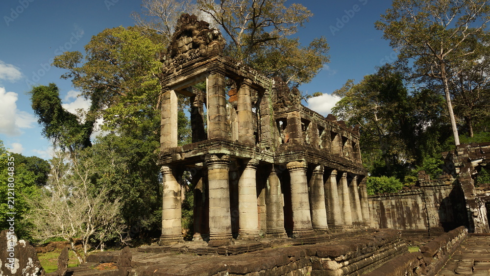 Obraz premium Ruins of a historic Khmer pavilion with classical columns under a blue sky, Angkor Wat archaeological park, Siem Reap