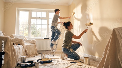 Young couple painting a room together with paint rollers and cans on a sunny day