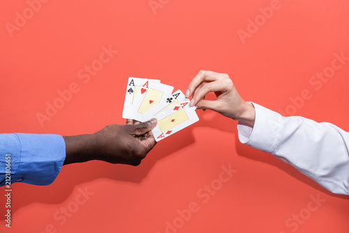 Hands exchange aces in a card game on coral background