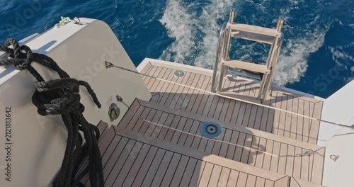 seething water from under a moving catamaran, crystal clear azure water, sea foam, ladder with ladder for descent into the water, wooden deck